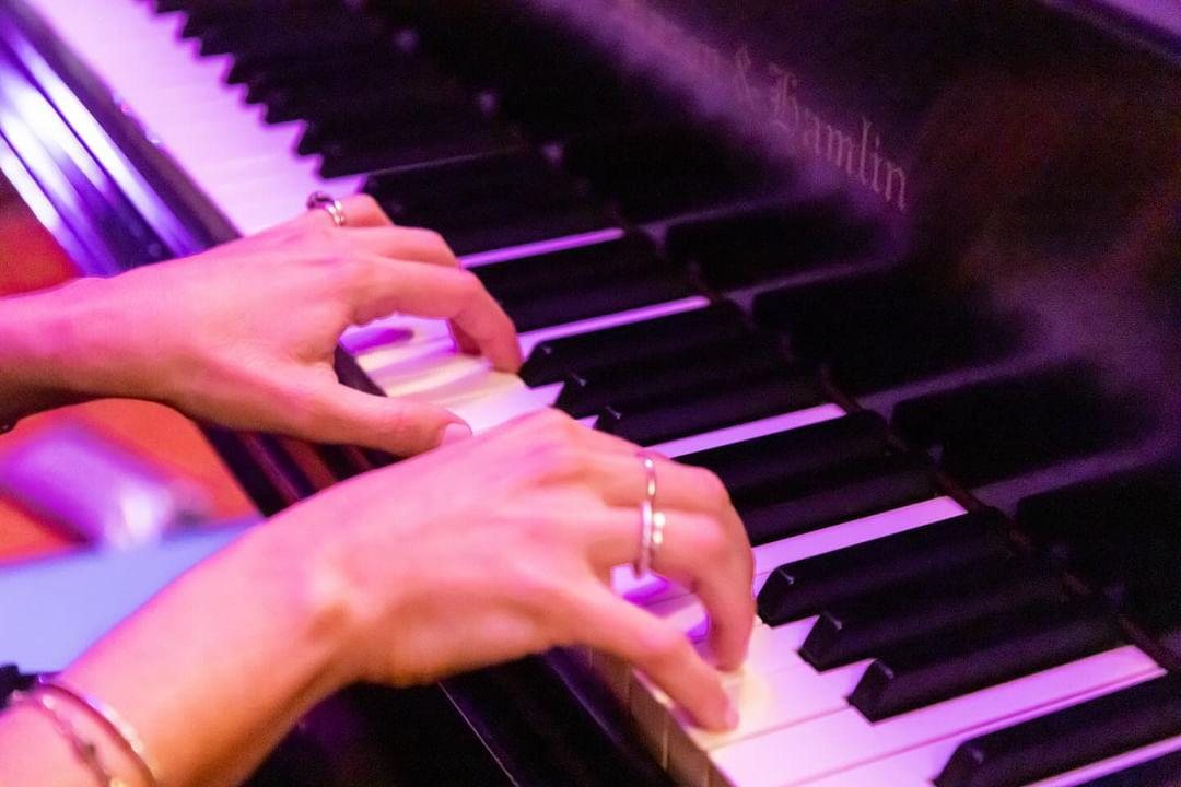 Manos tocando un piano iluminado con luces violetas