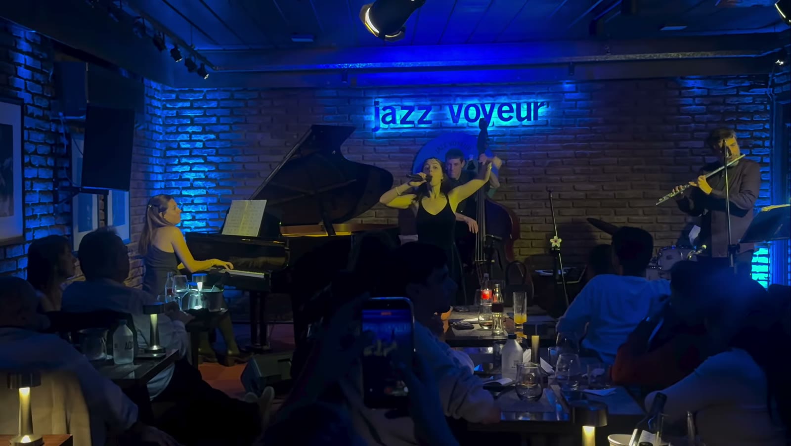 El salón durante un show: el piano a la izquierda, la banda al fondo y las mesas con velas frente al escenario